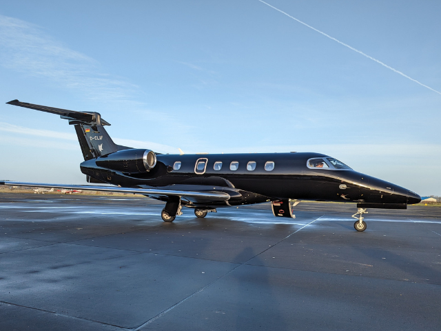 A black private jet parked on a runway under a clear blue sky.